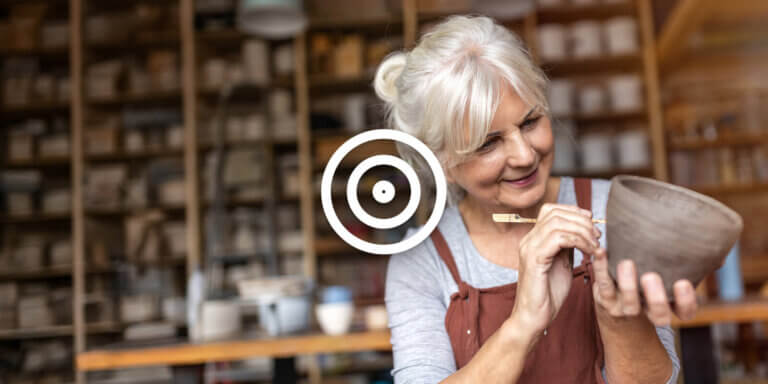 A woman with white hair smiling while craving something on a bowl.