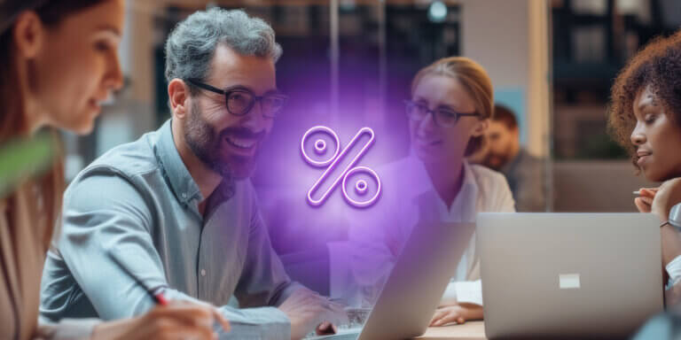 An image with a purple percentage symbol in the center showing a man with grey hair and black glasses smiling while using a laptop.