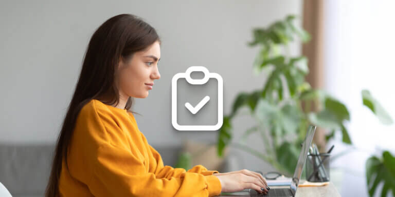 A visual showing a girl with long brown hair and wearing an orange sweater typing something on a laptop screen.