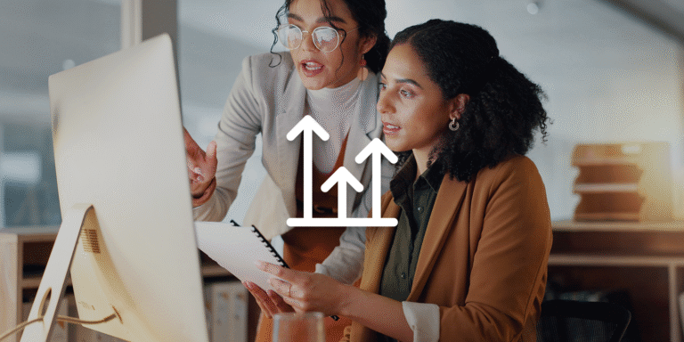 An image showing two women in a professional environment talking while looking at a computer screen.